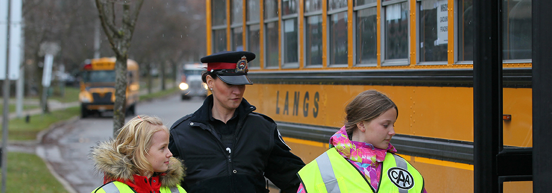 Female officer with 2 safety patrollers in front of school bus