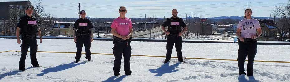 Five LPS officers standing on snow covered rooftop wearing pink shirts/badges
