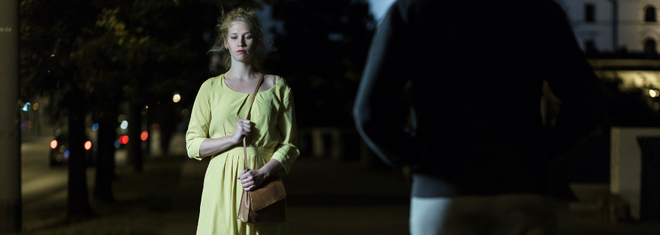 woman walking at night clutching purse, being approached by stranger in dark clothing
