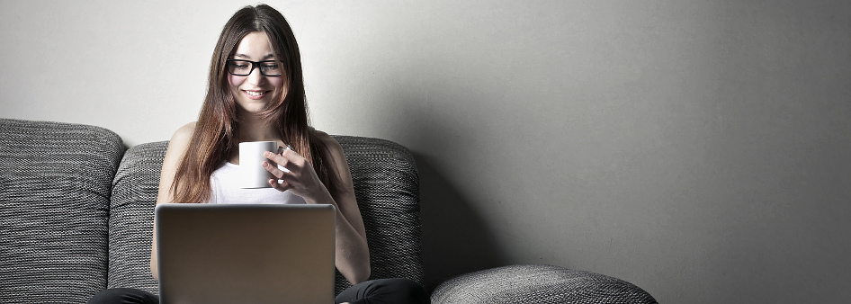 Woman with laptop on her lap, sitting on couch, drinking tea