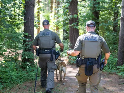 Two LPS K9 officers walking K9 through wooded area