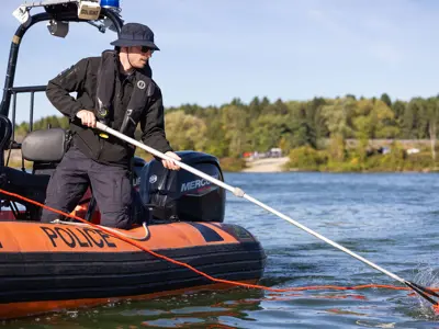 LPS officer in boat, retrieving item from water with long net
