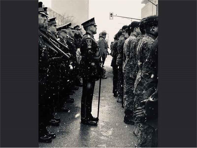 Black and White image of lone officer leading colour guard